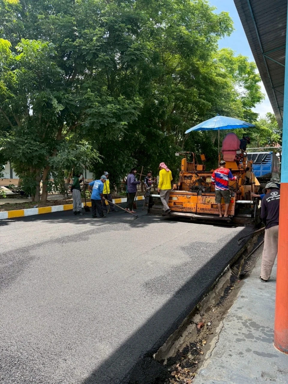 ภาพหน้างานลาดยางมะตอยและเครื่องปูยางข้างอาคารโรงเรียน