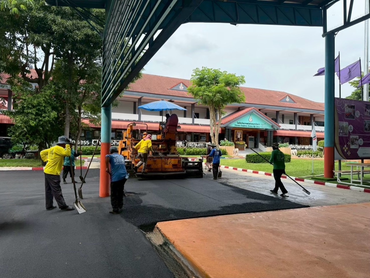 ภาพหน้างานทีมงานและเครื่องปูยางมะตอยใต้หลังคาบริเวณลานโรงเรียน